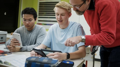 Zwei Jugendliche, die mithilfe einer pädagogischen Fachkraft konzentriert eine Aufgabe bearbeiten.