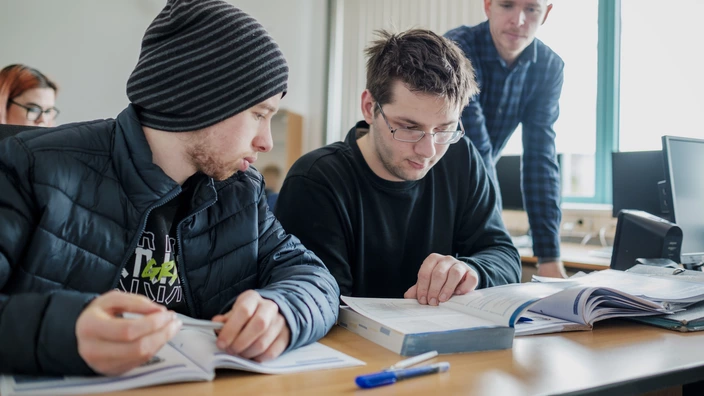 Zwei Jugendliche, die mithilfe einer pädagogischen Fachkraft konzentriert eine Aufgabe bearbeiten.